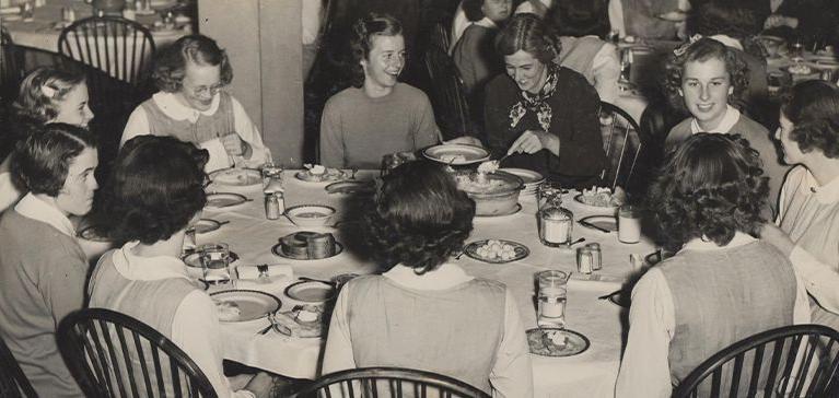 A group of girls sit around a table in a black and white photo of St. Margaret’s School for Girls.